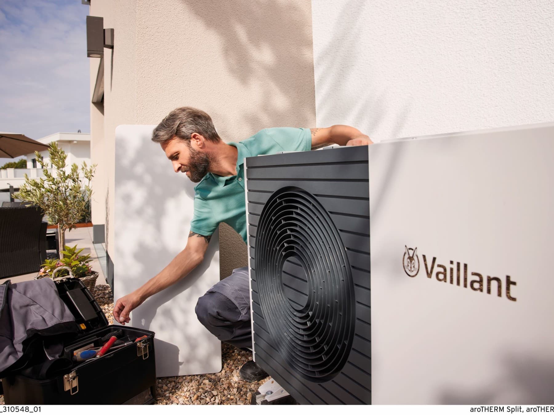 Instalator pracuje przy pompie ciepła zamontowanej przy budynku.