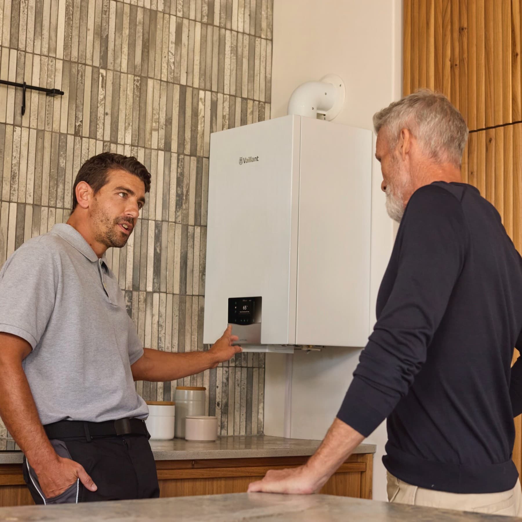Instalator wskazuje na kocioł i wyjaśnia coś klientowi